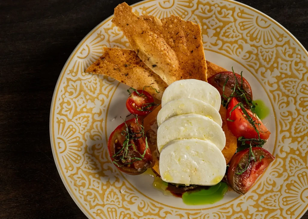 Fresh caprese salad with mozzarella, tomatoes, basil, bread, on decorative plate.