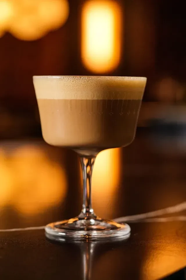 Creamy light brown drink with foam in an etched coupe glass.