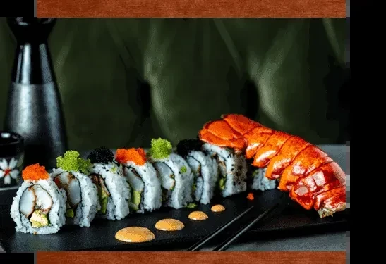 Sushi rolls and cooked lobster tail on a dark rectangular platter.