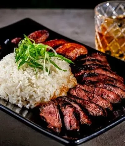 Grilled steak, rice with green onions, and cocktail on black plate.