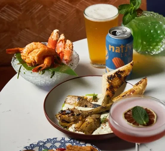 Table laden with seafood, beer, cocktails, and grilled artichoke hearts.