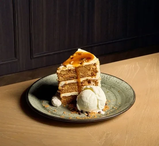 Multi-layered cake slice with caramel, nuts, and a scoop of ice cream.