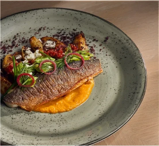Crispy pan-seared fish, orange puree, roasted vegetables, artfully plated.