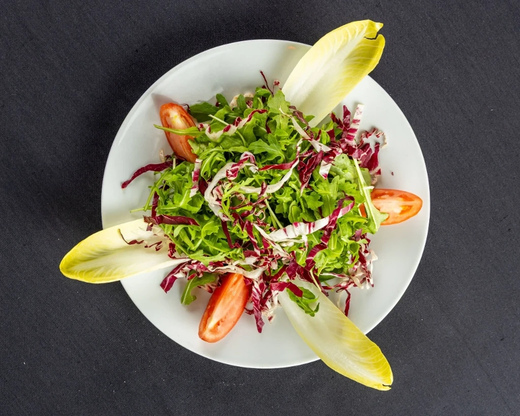 Overhead salad of arugula, radicchio, tomato, and endive on white plate.