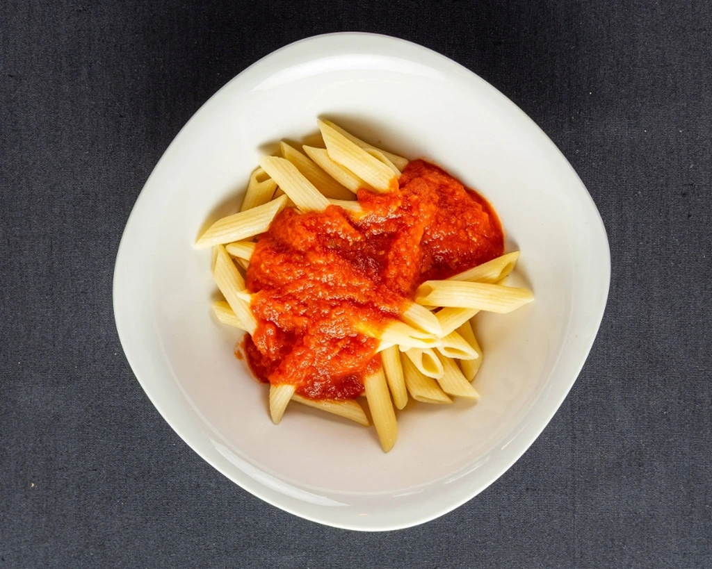 Penne pasta with chunky tomato sauce in a modern white bowl.