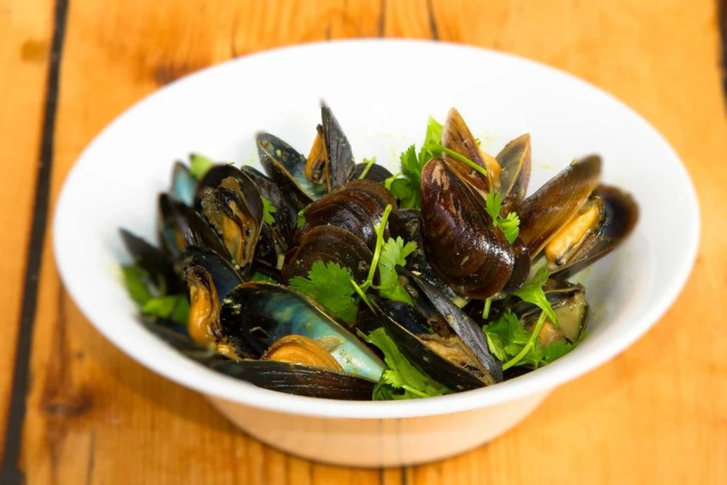 Cooked mussels in white bowl with cilantro on a wooden table.
