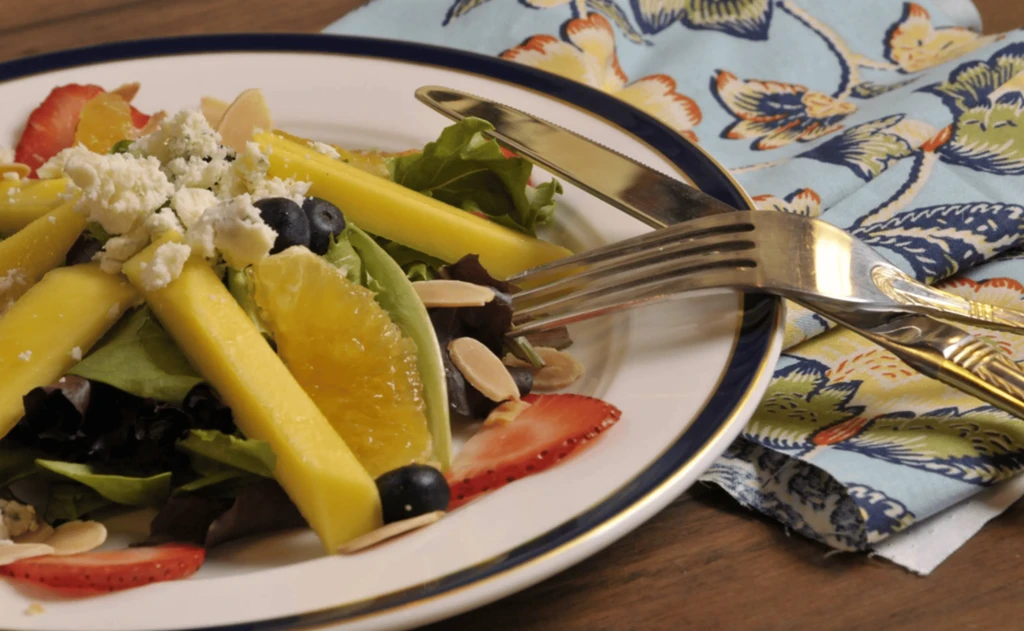 Fresh, colorful salad with fruit, cheese, and nuts on a white plate.