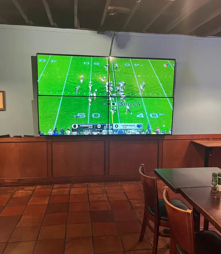 Large video wall shows live football in a casual sports bar.