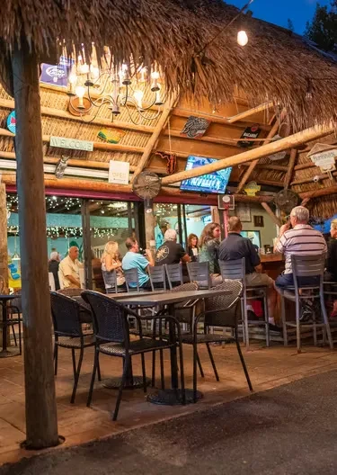 Thatched-roof outdoor bar at night with people and warm lighting.