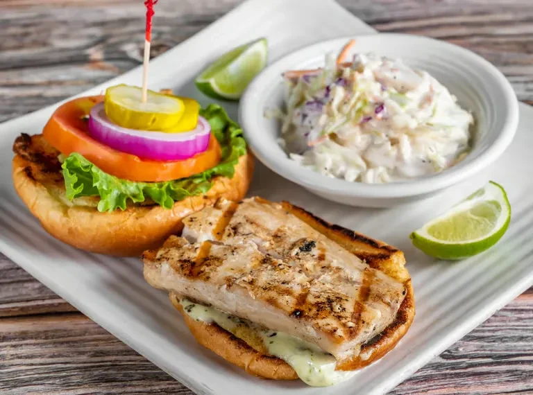 Open-faced grilled fish sandwich, coleslaw, and lime wedges on a plate.