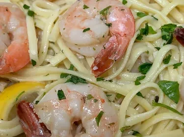 Close-up of linguine with large cooked shrimp, fresh herbs, and lemon.