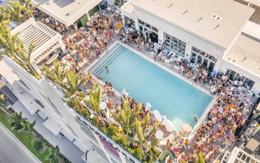 Aerial view of a lively rooftop pool party with people and floats.