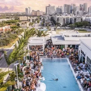 Aerial view: bustling rooftop pool party, city skyline at dusk.