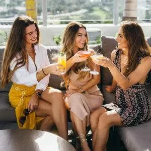 Three smiling women holding cocktails at an outdoor rooftop bar.