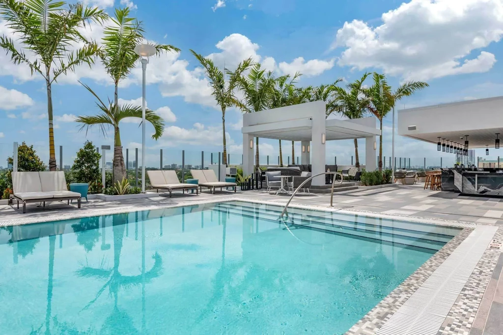 Sunny rooftop pool, lounge chairs, bar, pergola, and urban skyline.