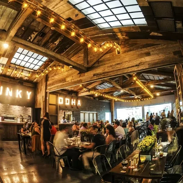 Lively rustic-industrial bar interior with "FUNKY DOHA" sign and patrons.