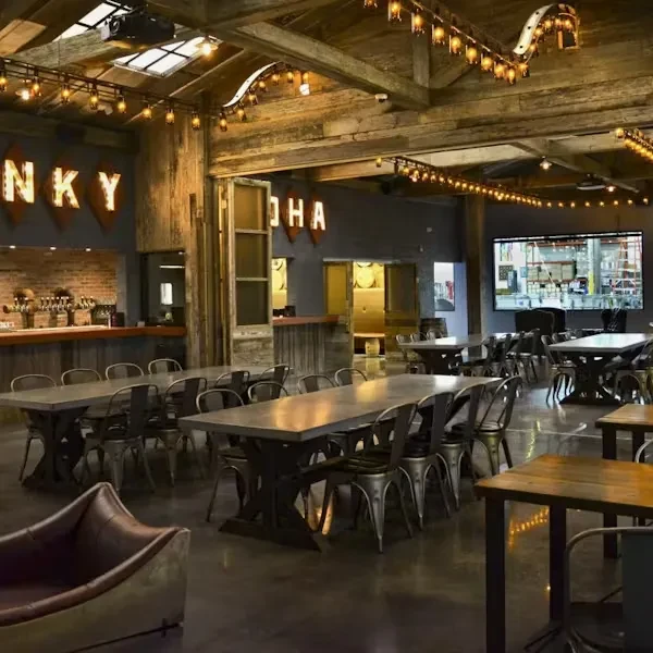 Spacious rustic industrial restaurant interior with long tables and a bar.