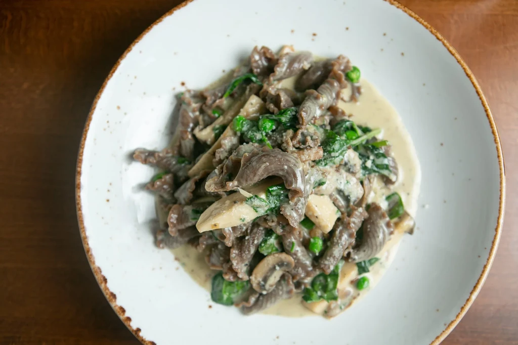 Plate of dark pasta with creamy sauce, spinach, peas, and mushrooms.