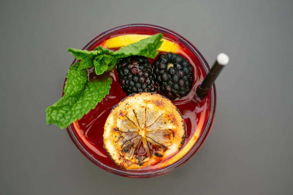 Crimson drink, blackberries, grilled lemon, mint, and straw, from above.