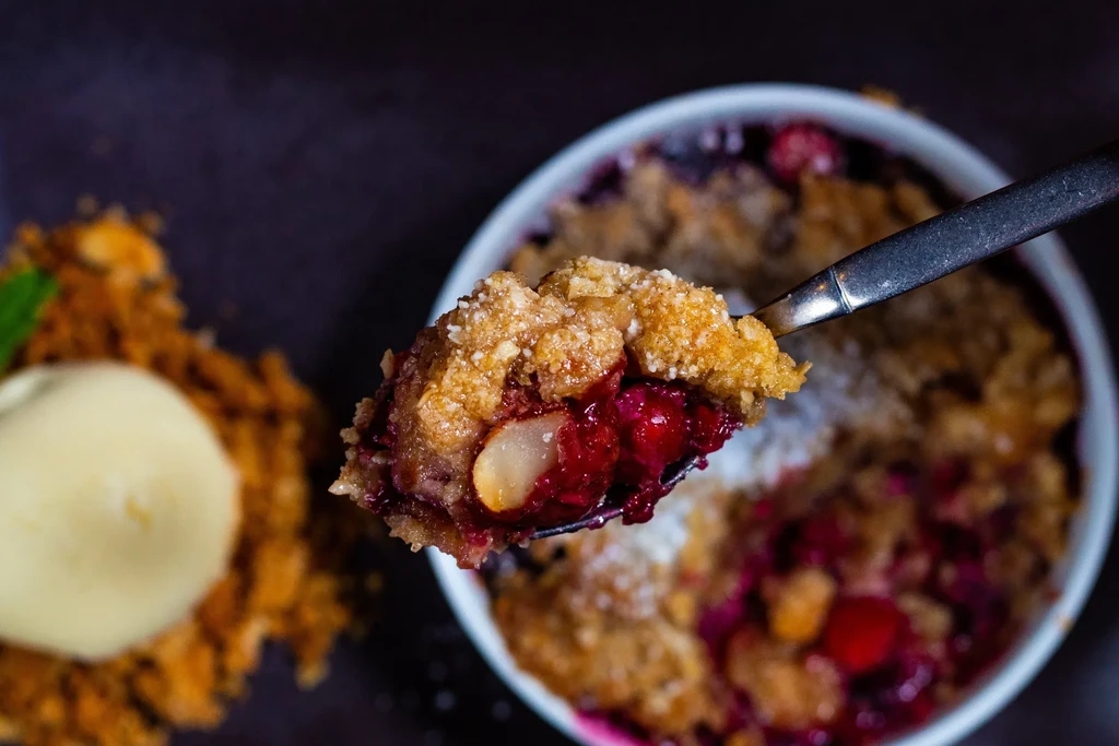 Golden oat crumble spoonful with red berries and vanilla ice cream.