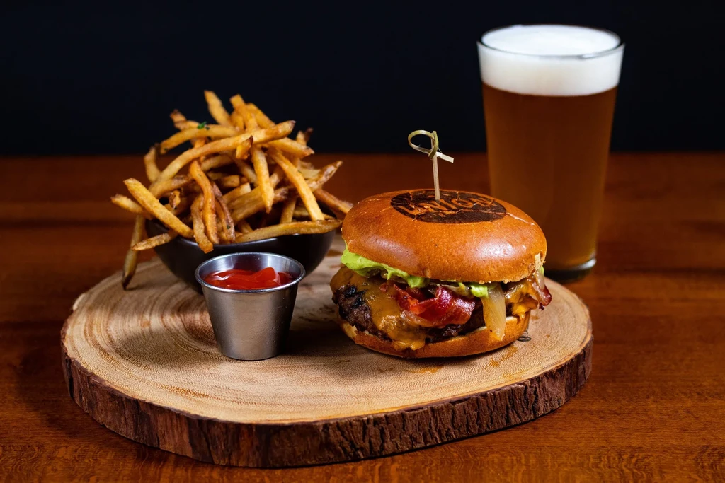A gourmet burger, fries, and beer artfully arranged on a wooden board.