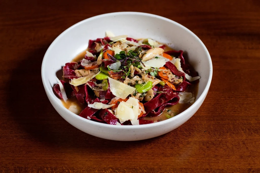 Top-down red pasta dish with Parmesan, edamame, shredded meat, carrots.