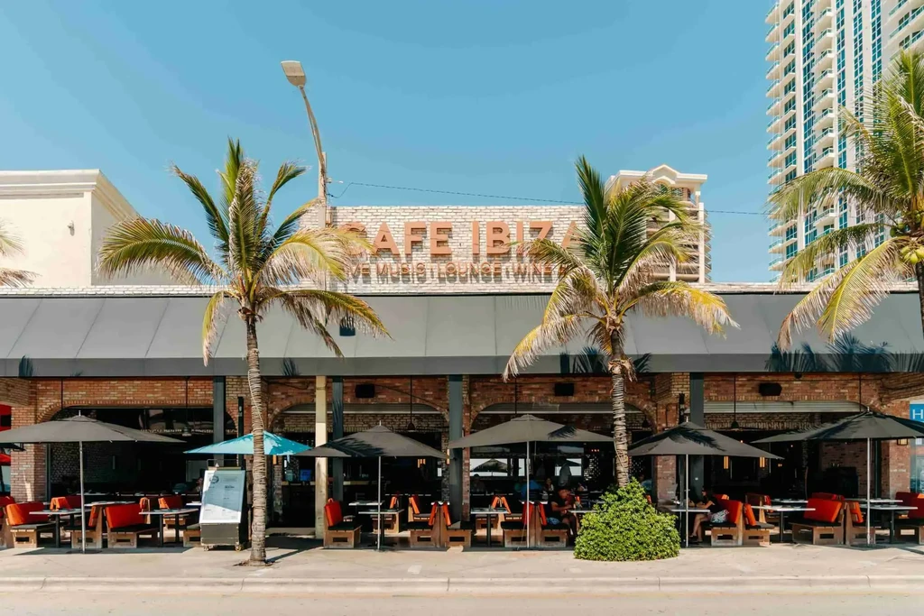 Cafe Ibiza exterior with outdoor dining, palm trees, and people.