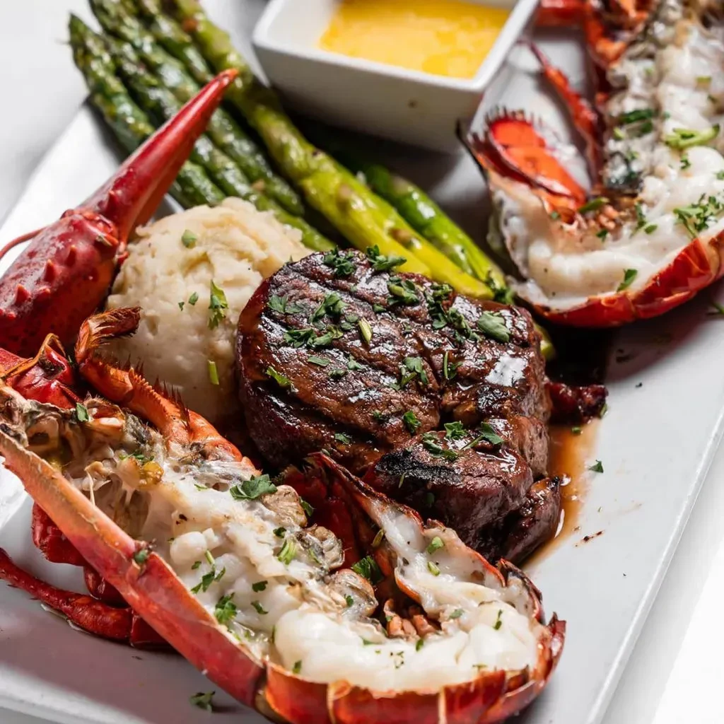 Grilled steak, lobster tails, mashed potatoes, asparagus, and sauce.