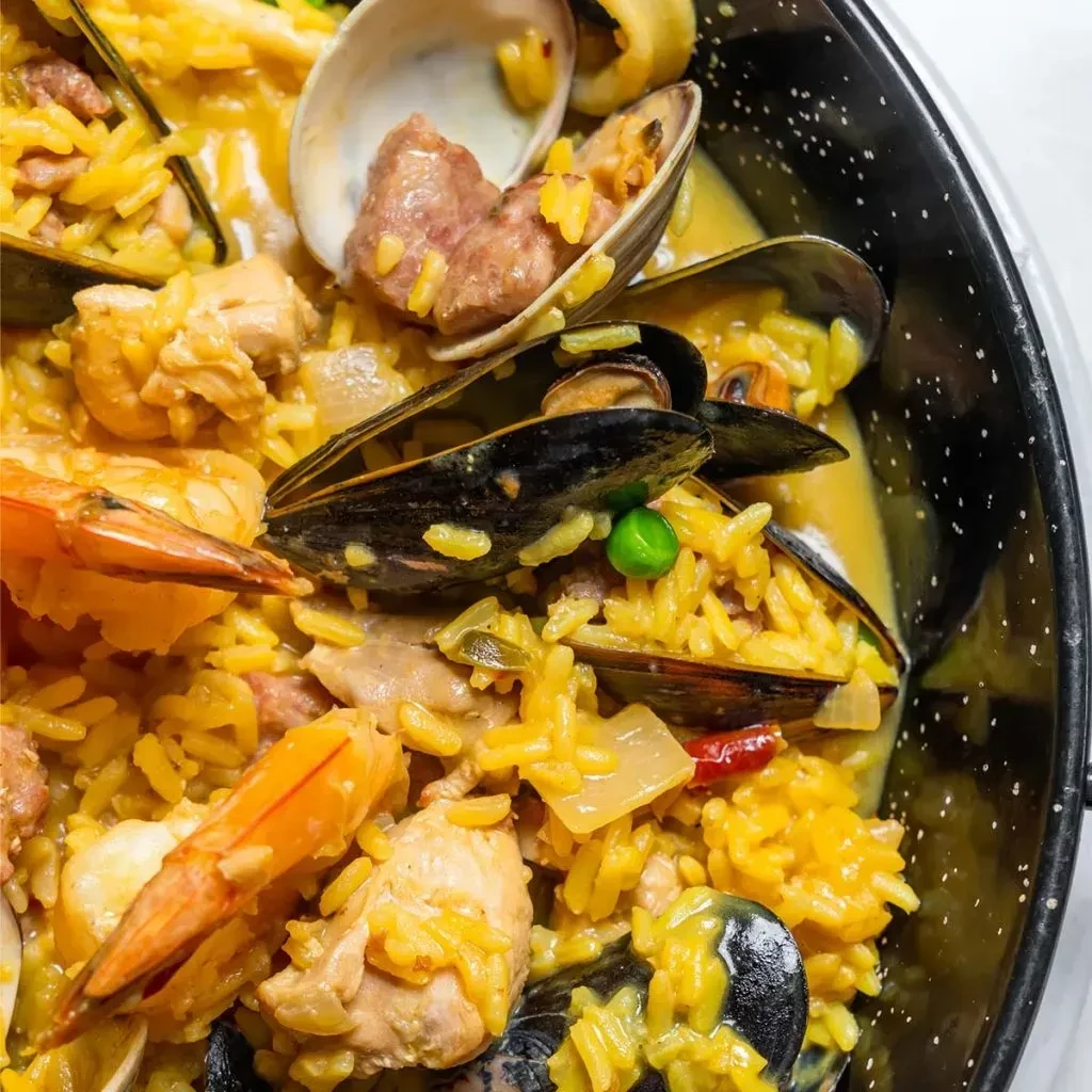 Close-up paella with chicken, mussels, clams, shrimp in a dark pan.