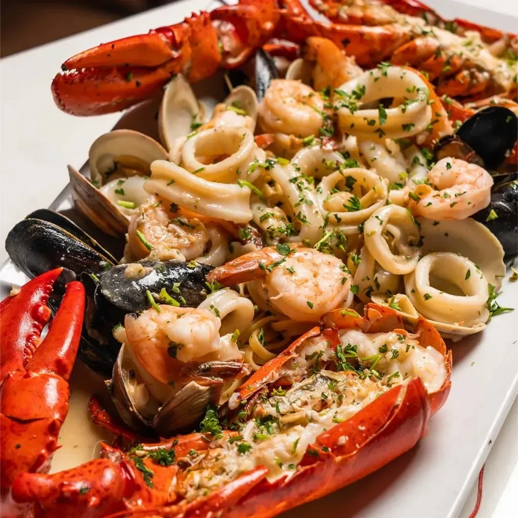 Vibrant seafood pasta platter with lobster, shrimp, mussels, calamari, and herbs.