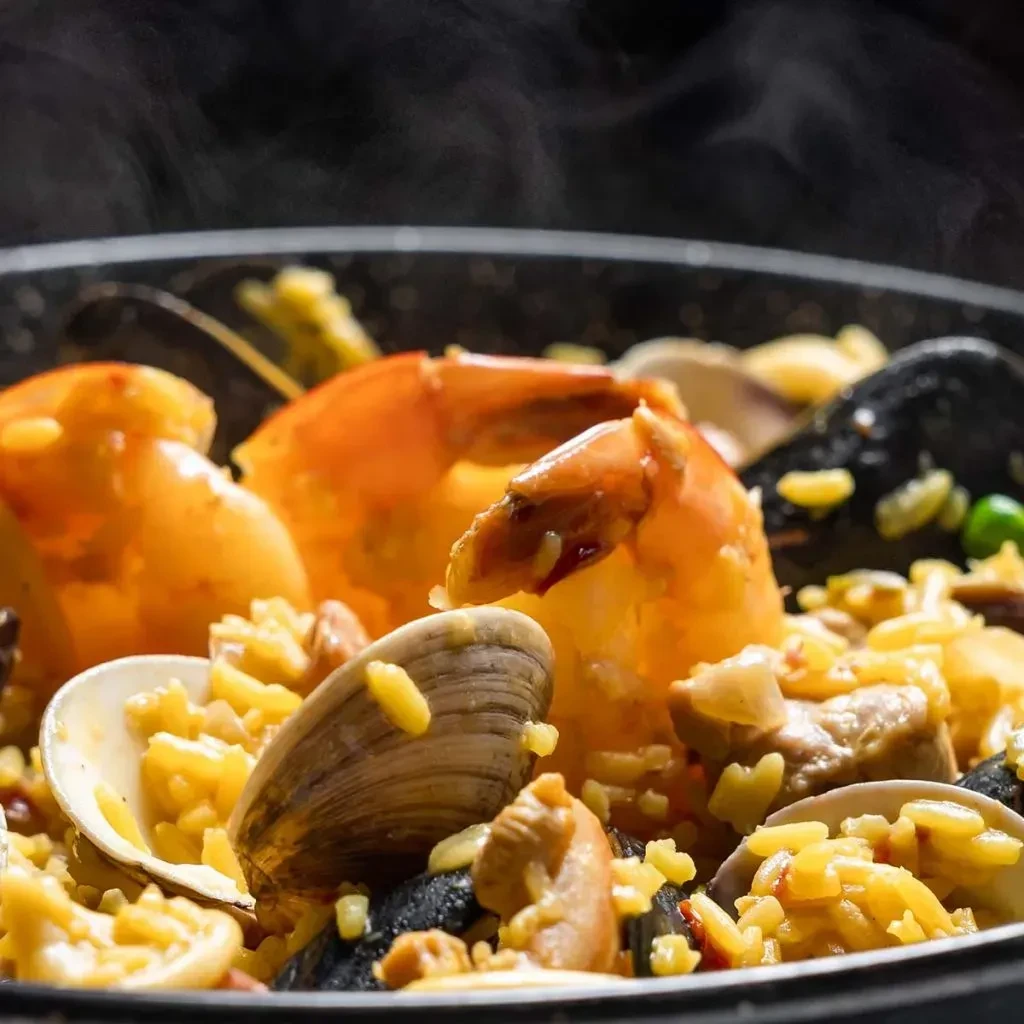 Steaming seafood paella with shrimp, mussels, clams, and yellow rice.