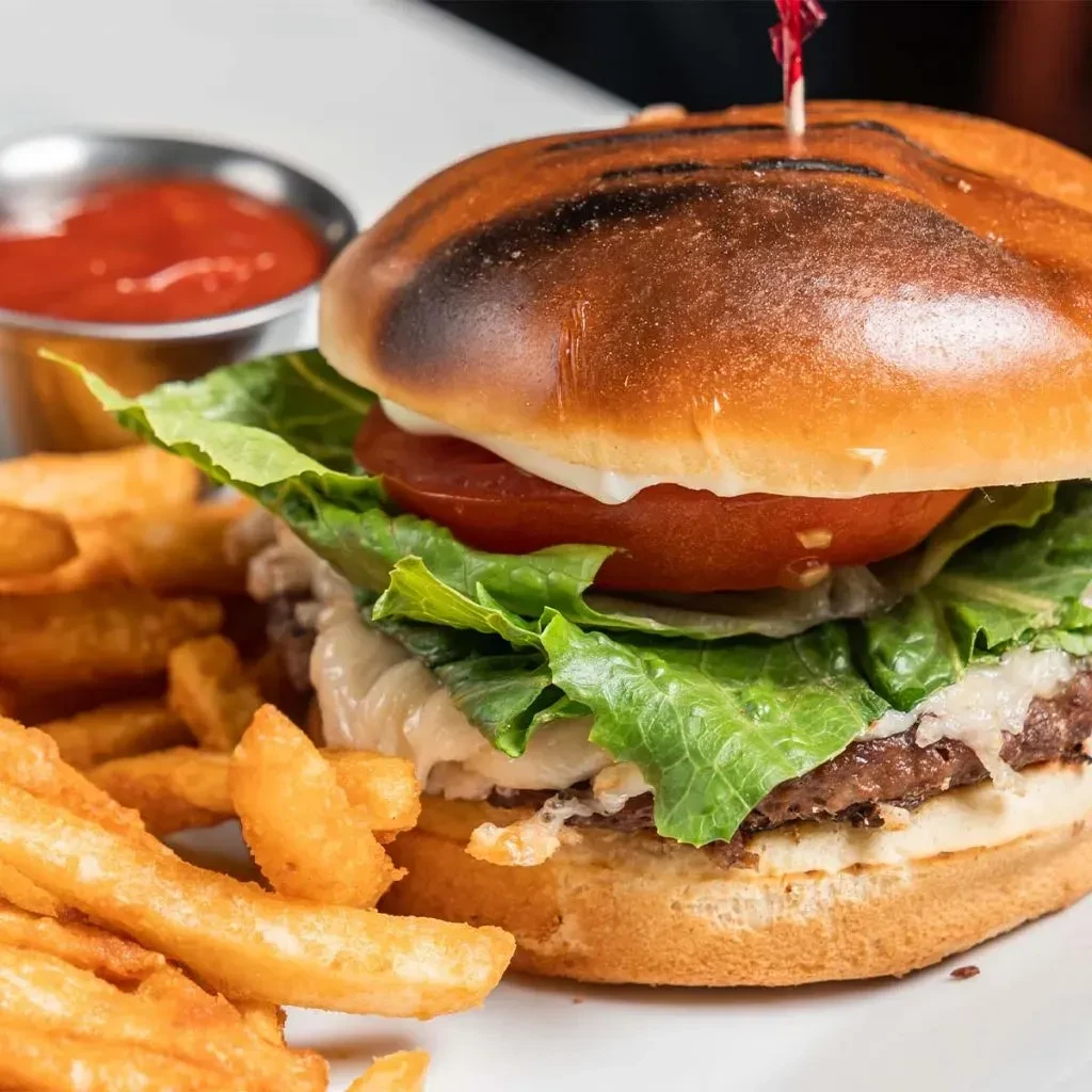 Gourmet burger, golden fries, and ketchup on a white plate.