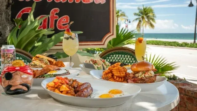 Outdoor cafe table with diverse brunch, cocktails, and a beach view.