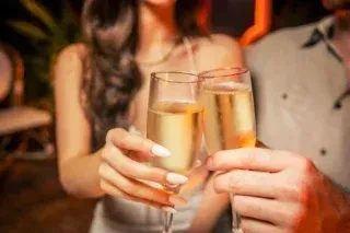 Two hands clinking champagne flutes with golden liquid.