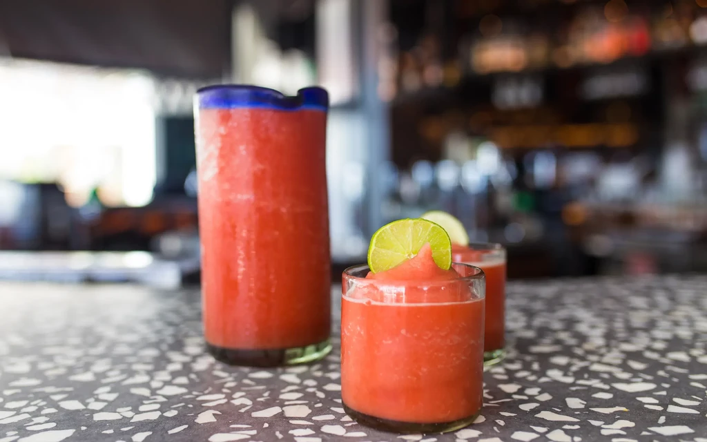 Red frozen drinks in pitcher and two glasses with lime.