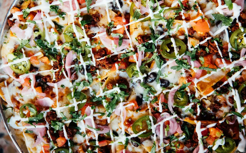 Close-up of loaded nachos with melted cheese, meat, and colorful toppings.