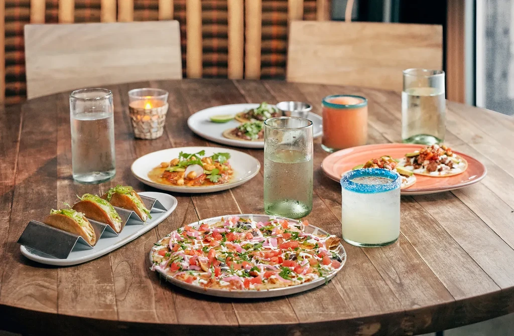 Restaurant table with hard-shell tacos, loaded nachos, drinks, and a candle.