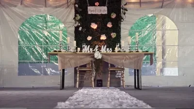 Sweetheart table with 'Mr & Mrs' sign, floral backdrop, and rose petals.