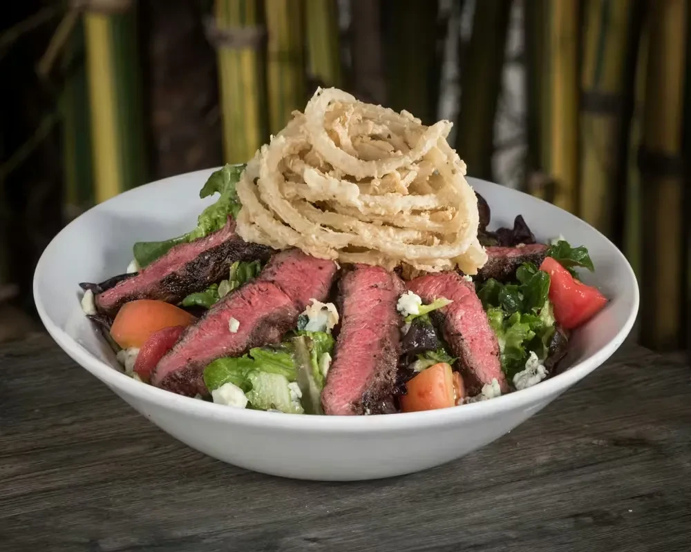 Grilled steak salad with mixed greens, cheese, and crispy onion rings.