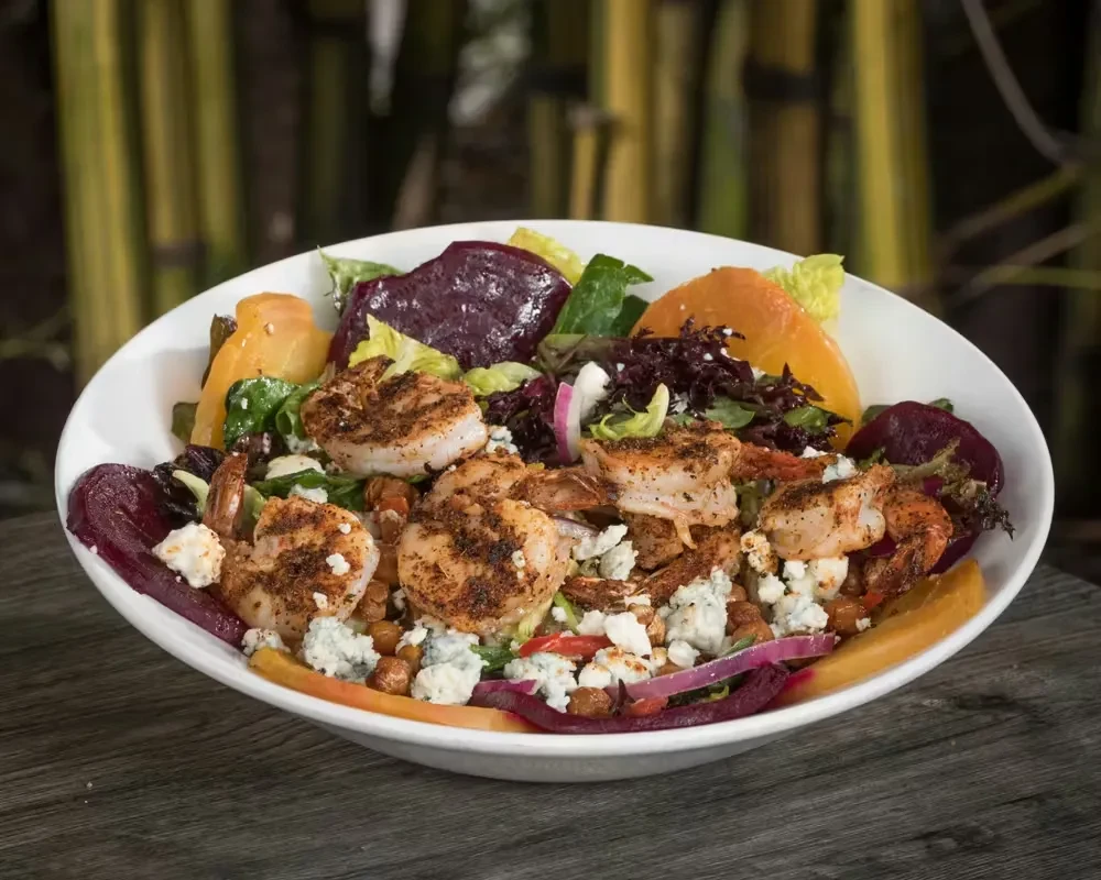 Vibrant salad with grilled shrimp, beets, blue cheese, on a wooden table.