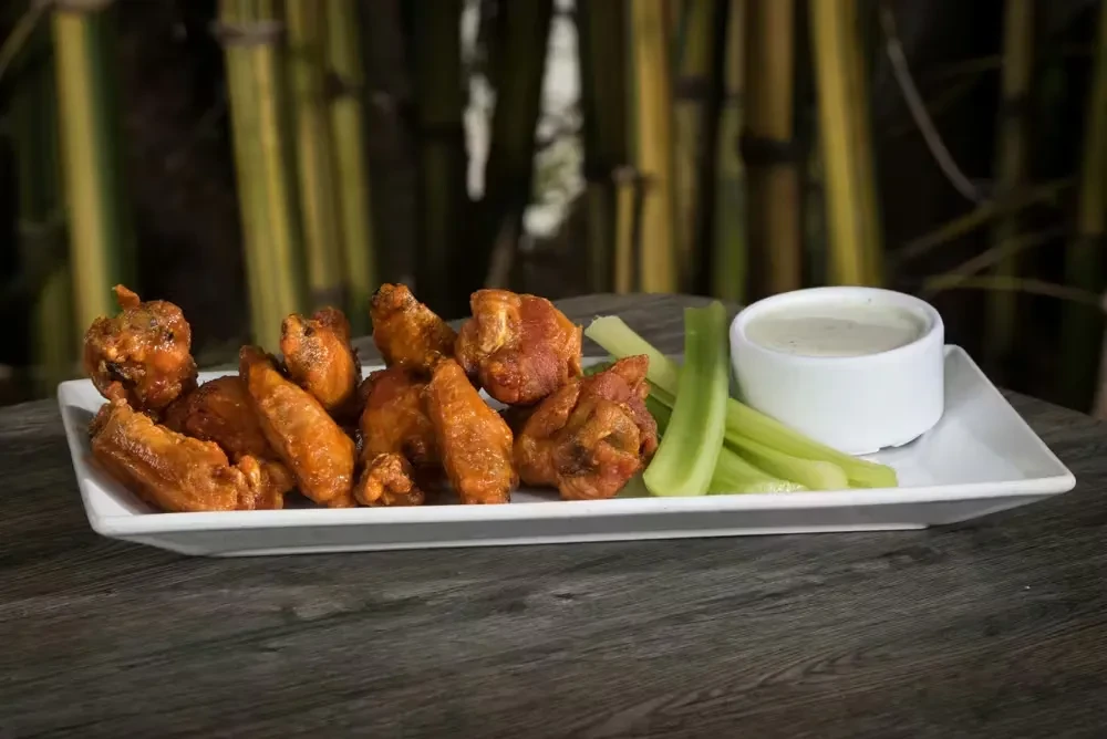 A platter of saucy chicken wings, green celery, and creamy dip.