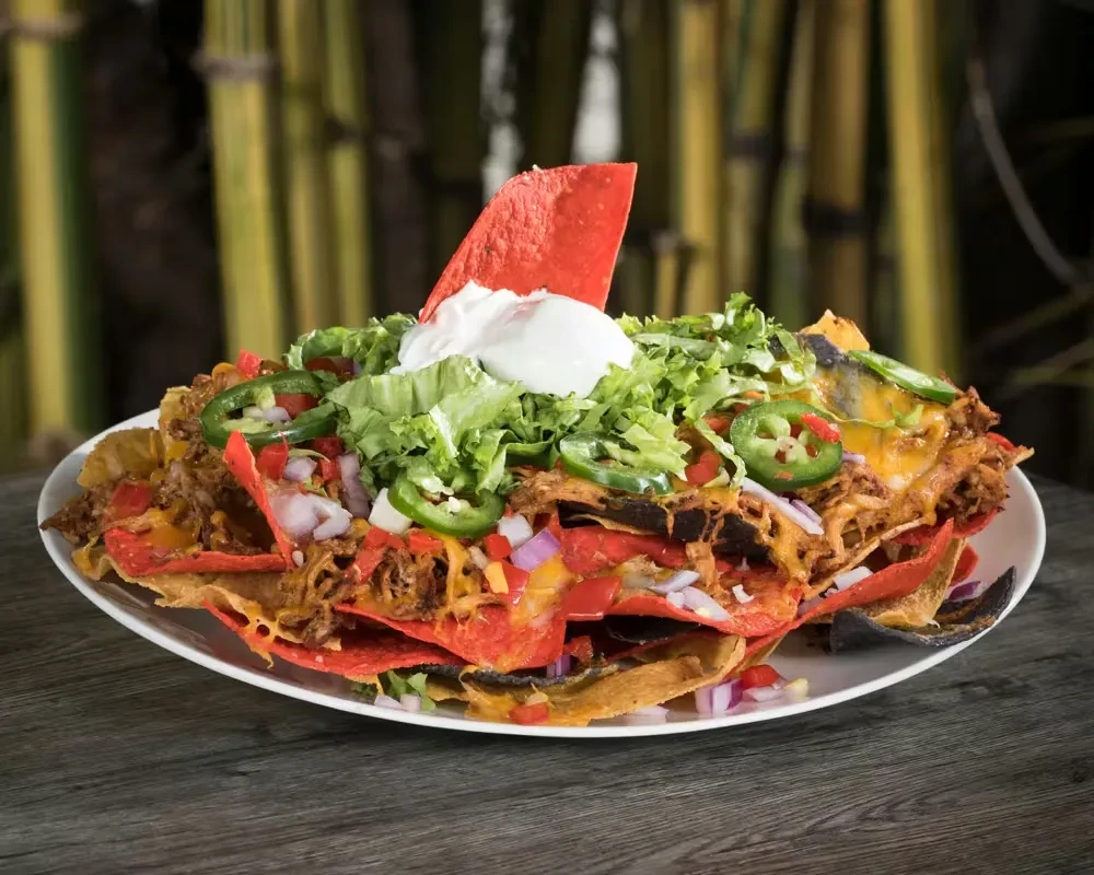 Large nachos piled high with meat, cheese, vegetables, and sour cream.