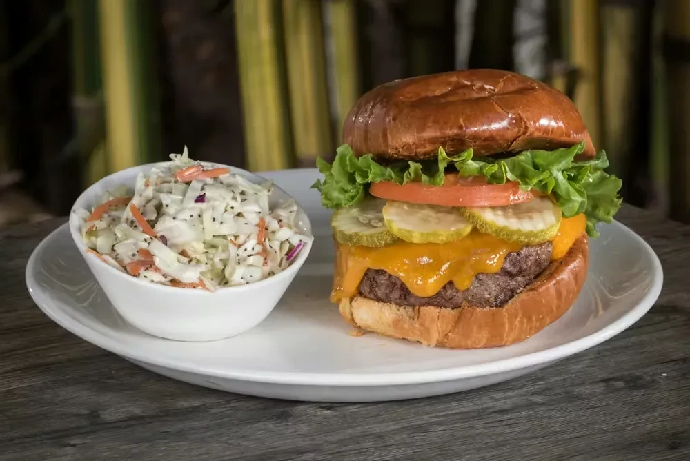 Close-up of a gourmet cheeseburger with coleslaw on a wooden table.