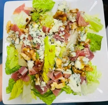 Close-up salad with lettuce, blue cheese, cured meat, walnuts, balsamic glaze.