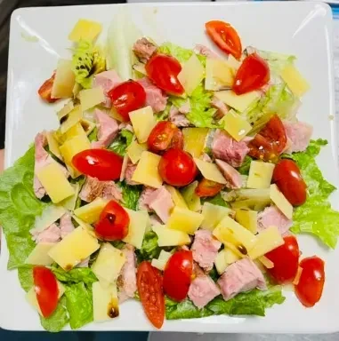 Overhead view of a salad with lettuce, tomatoes, cheese, and ham.