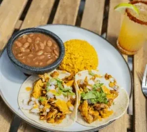 Tacos, beans, rice, and margarita served on a wooden outdoor table.