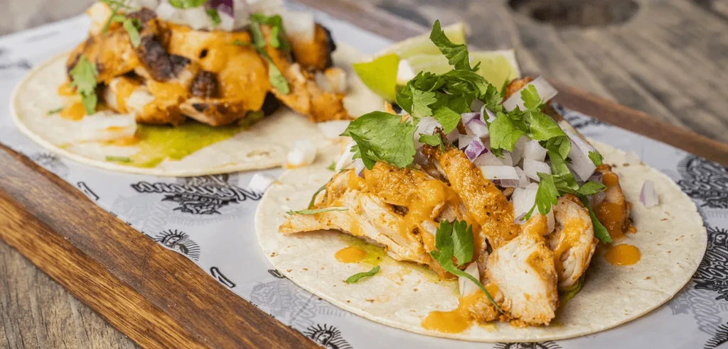 Two chicken tacos on a branded paper liner and wooden tray.