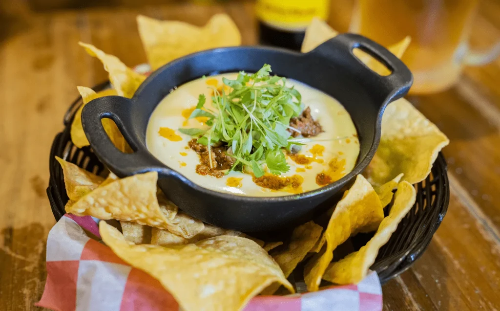 Queso dip with meat and cilantro in skillet, with tortilla chips.