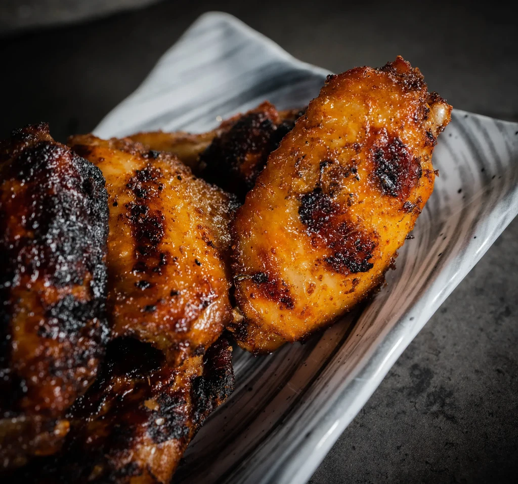 Crispy, glazed chicken wings with char marks served in dish.