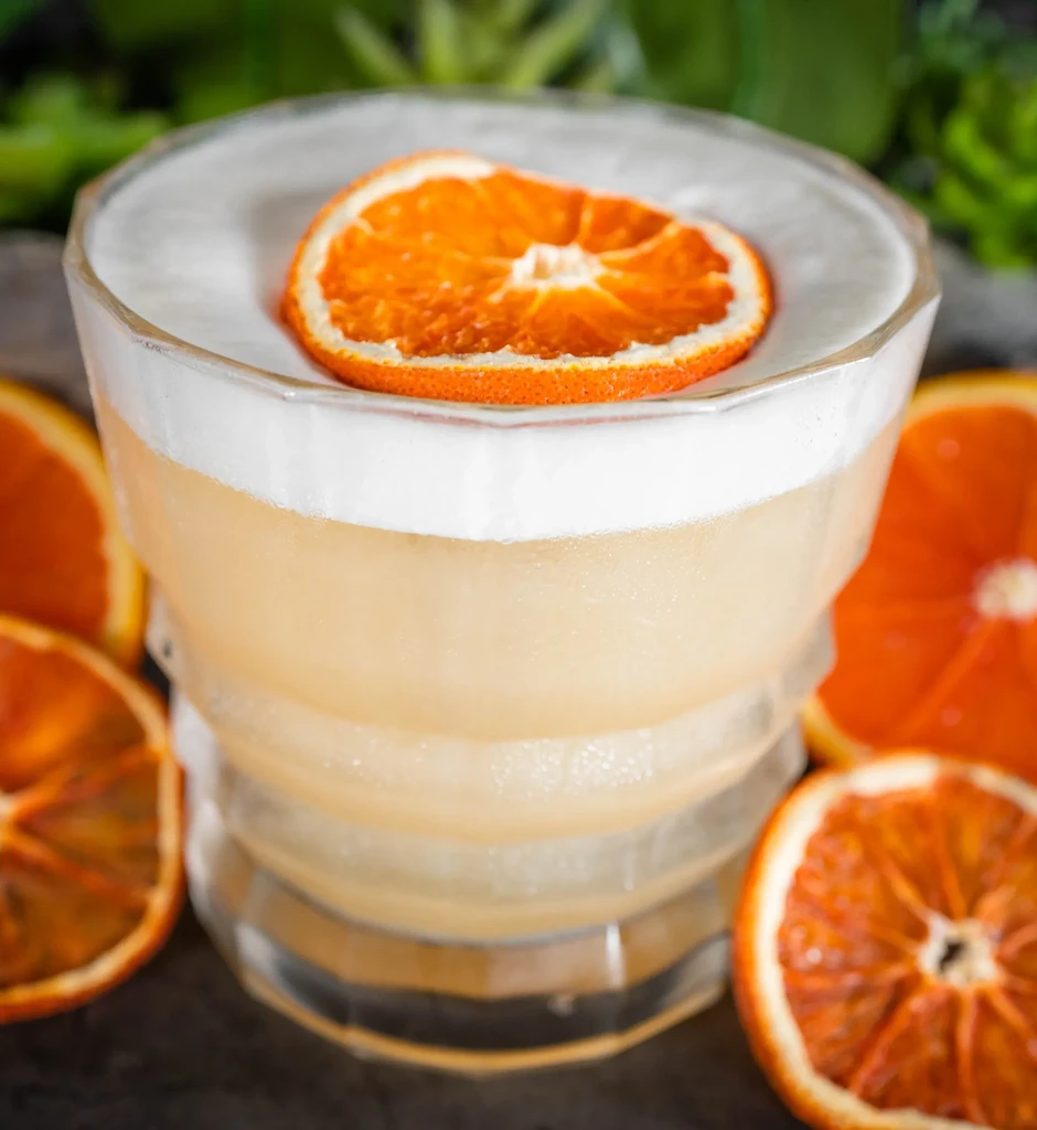 Two-layered cocktail in faceted glass with a dried orange slice.